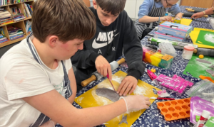 Two young people use a cutting board to prepare baking decorations.