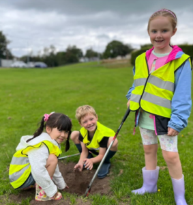 Three young people wearing yellow safety vests pose with litter-picking equipment.